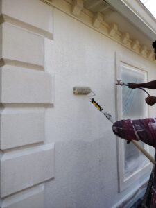 using a paint roller to paint the exterior of a house